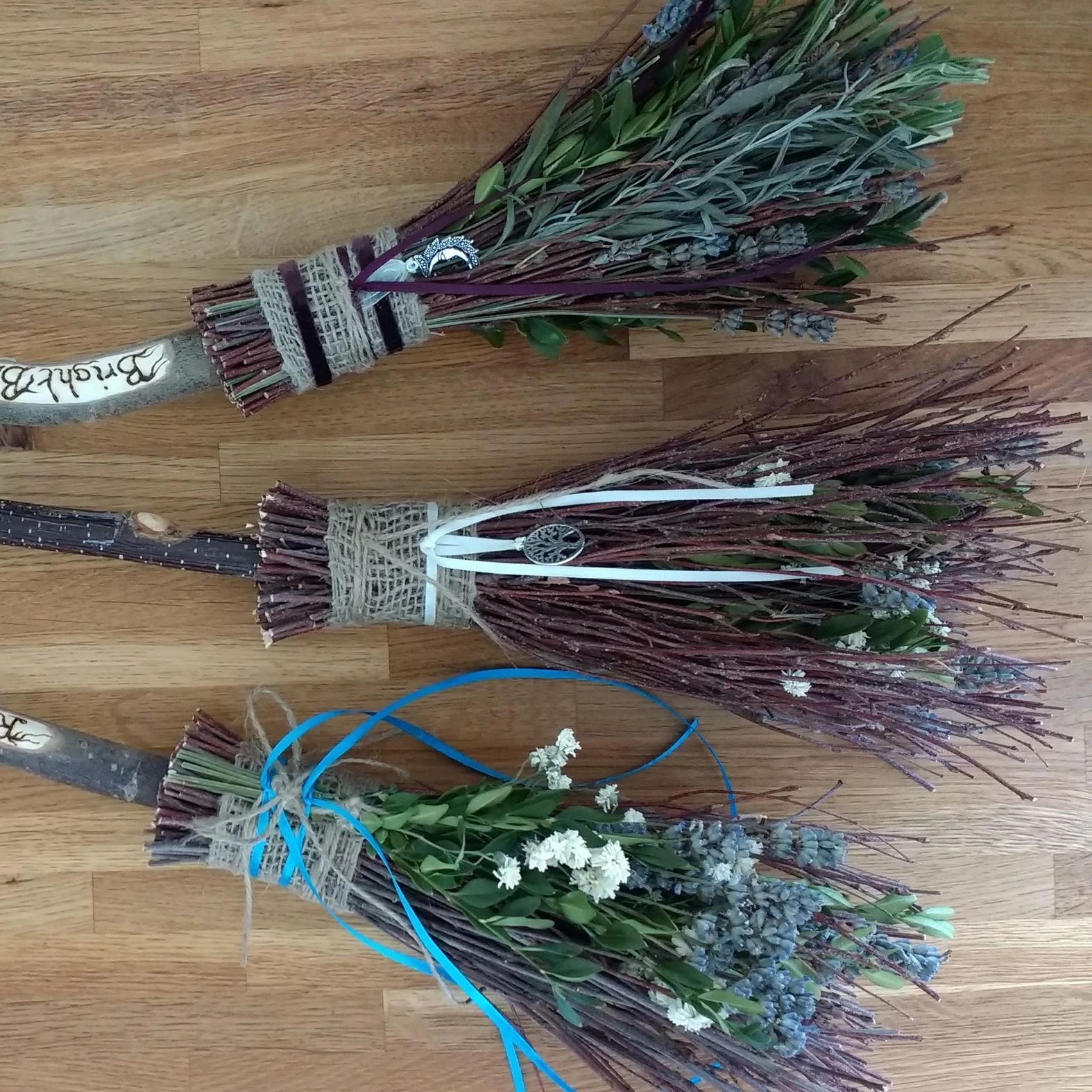 Three decorative bundles of twigs, herbs, and flowers tied with ribbons and twine on a wooden surface.