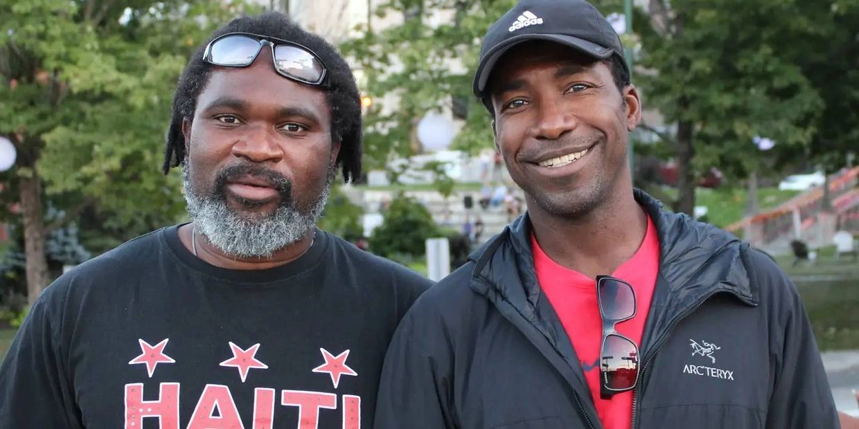 Deux hommes souriants posent en extérieur.
