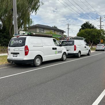 Two white Vivo service vans parked on a suburban street with equipment on their roofs.