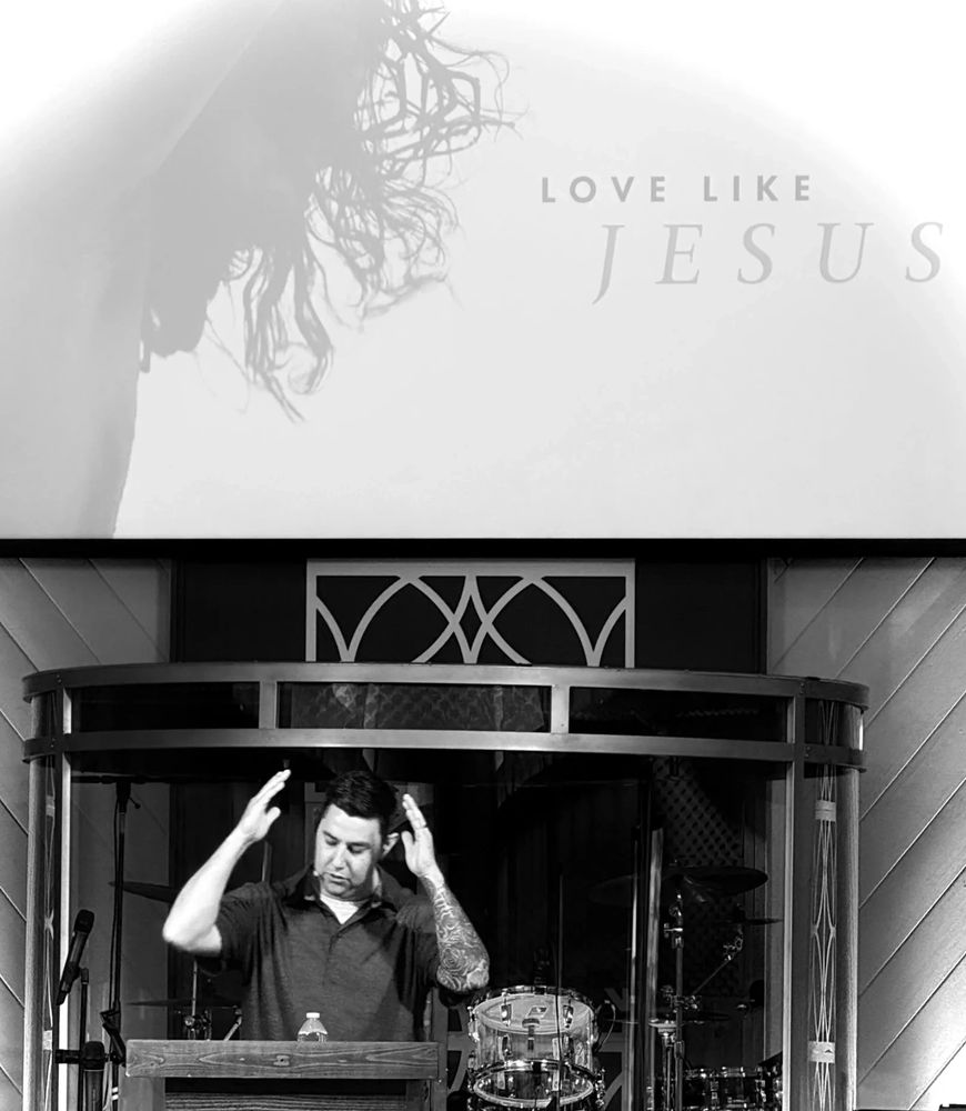 Man speaking at a church with a 'Love Like Jesus' sign.