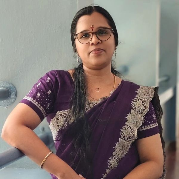 Woman in a purple embroidered saree wearing glasses and earrings.
