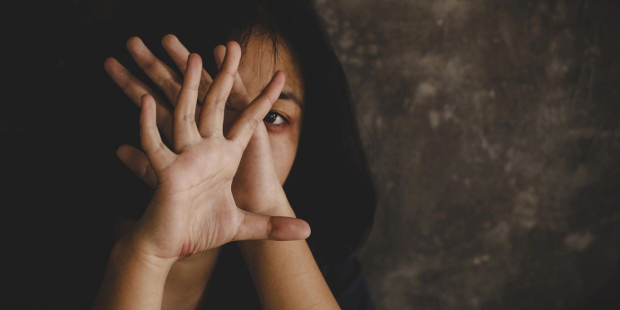 Person hiding face behind hands with dark background.