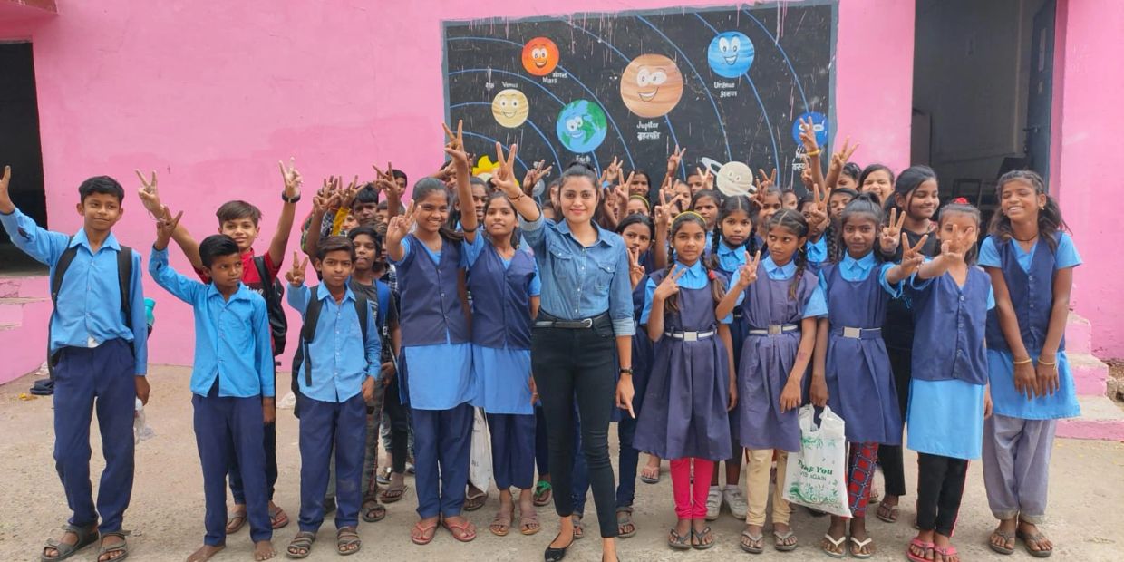 Group of school children and a teacher posing with peace signs.