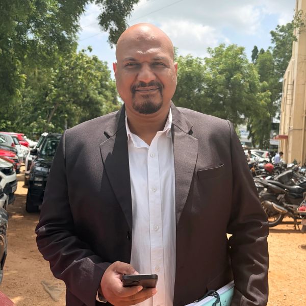Man in a suit holding a phone outdoors.