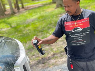 Man detailing a white car with spray in an outdoor setting.