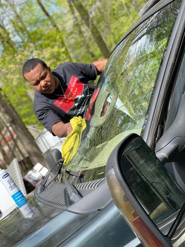 A man cleaning a car windshield with a yellow cloth outdoors.
