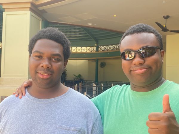 Two men posing happily, one giving a thumbs up.
