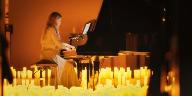 Frau spielt Klavier umgeben von Kerzenlicht.