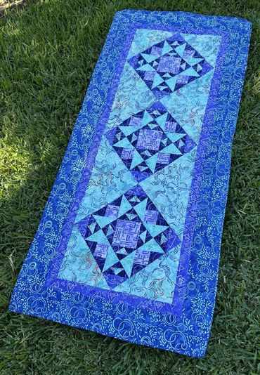 Blue quilt with geometric patterns laid on grass.