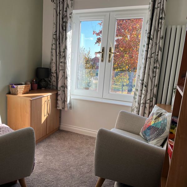 A room with two chairs facing a large window with an autumnal tree as the view