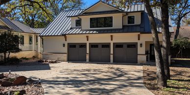 Completed residential garage with upstairs living space, metal roof and three garage doors.