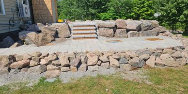 Stone patio with stairs and surrounding rock walls on a sunny day.