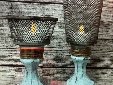 Rustic candle holders with wire mesh covers on distressed white wooden bases.