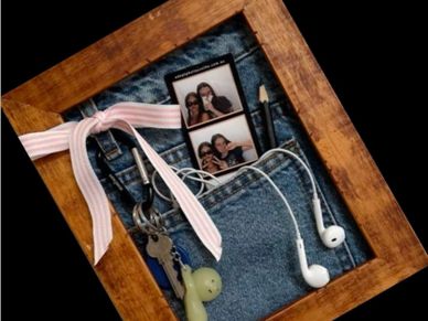 A wooden frame holding keys, earphones, and a photo strip on denim fabric.