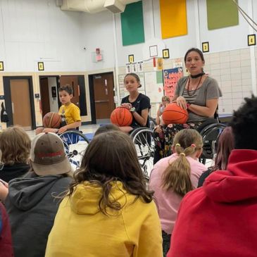 Three wheelchair basketball players speaking to a seated audience of children.