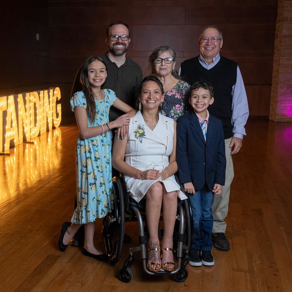 Patty and her parents, her partner, and her two kids pose for a picture with marquee lights behind 