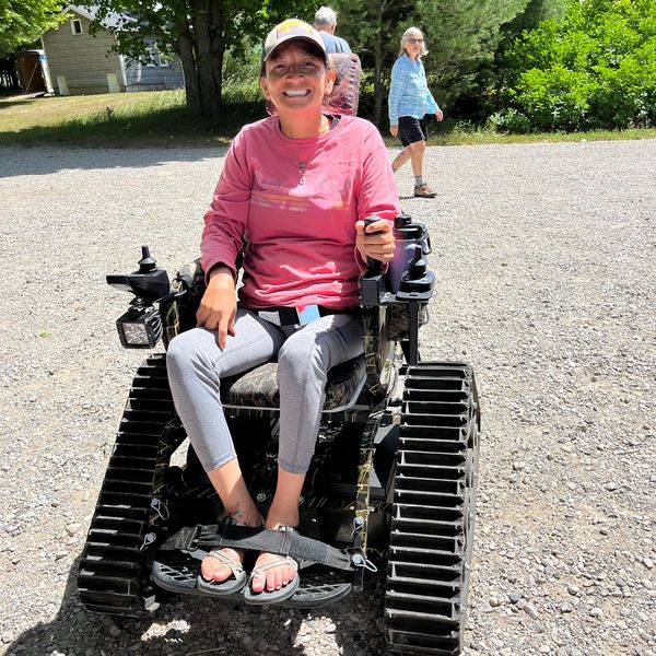 Patty is smiling and sitting in an off-road trek chair with large triangular wheels. 