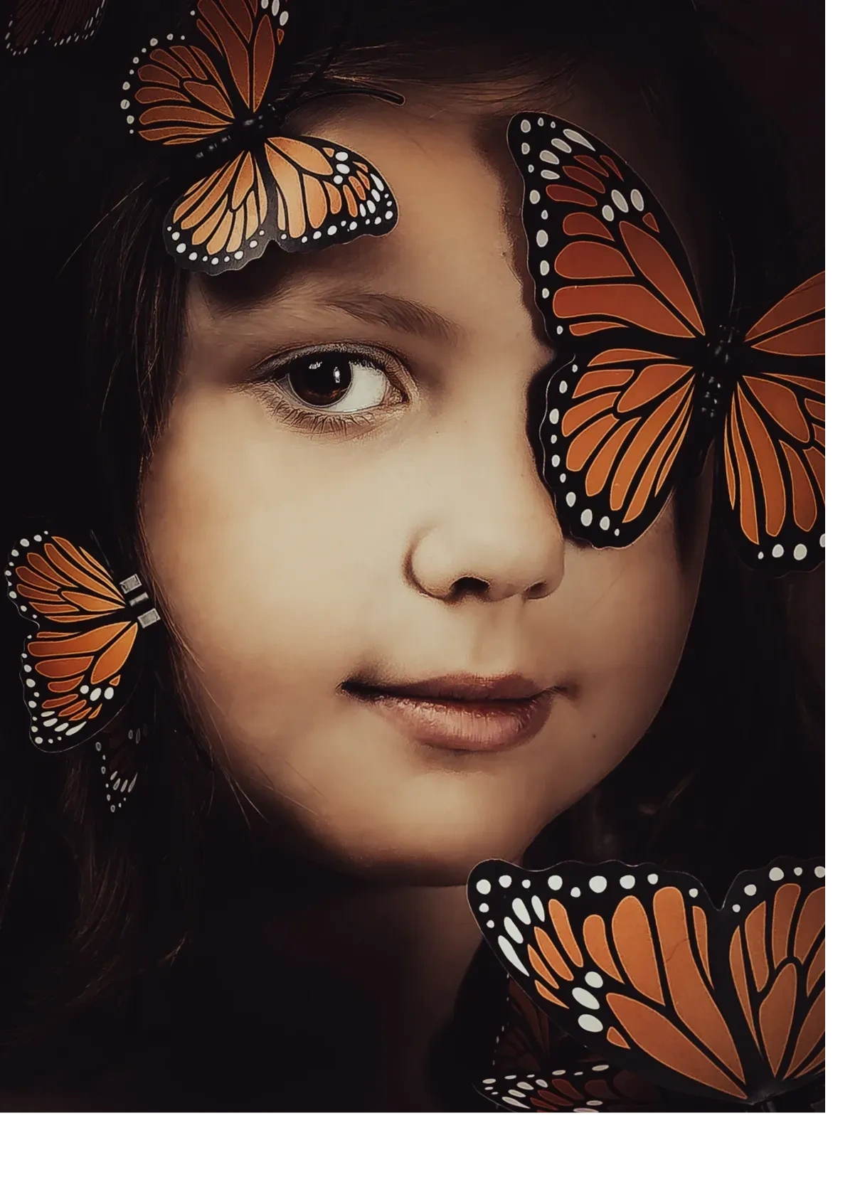 Fine art portrait of a young girl covered in monarch butterflies, looking into camera.  