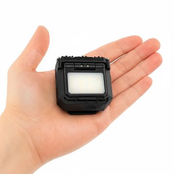 Compact black LED light held in a person's hand for size reference.