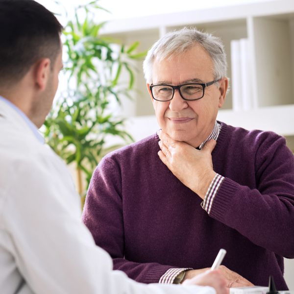 Senior man discussing throat pain with doctor during consultation.