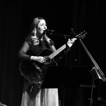 Kobieta śpiewająca i grająca na gitarze na scenie.