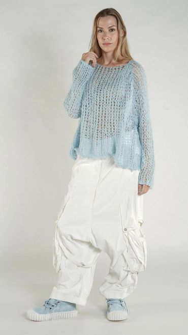 Woman in light blue knit sweater and loose white pants posing.