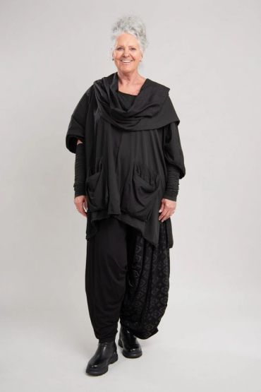 Une femme âgée portant une tenue noire ample sourit.