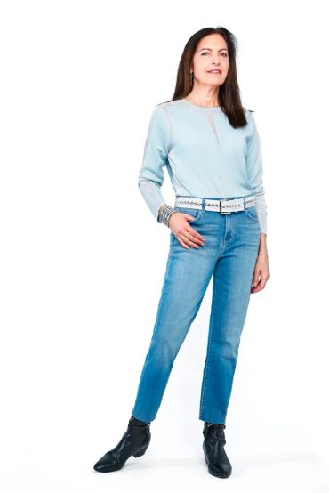 Woman in light blue top and jeans posing confidently.