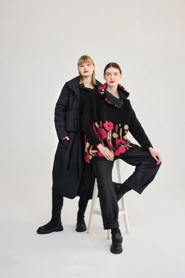 Two women in stylish black outfits against a plain background.
