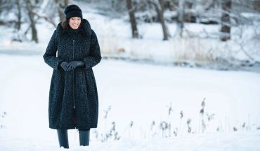 Woman smiling in winter coat and hat in snowy landscape.