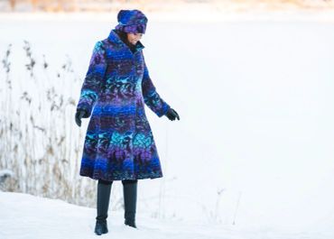 Person wearing blue patterned coat and hat in snowy landscape.