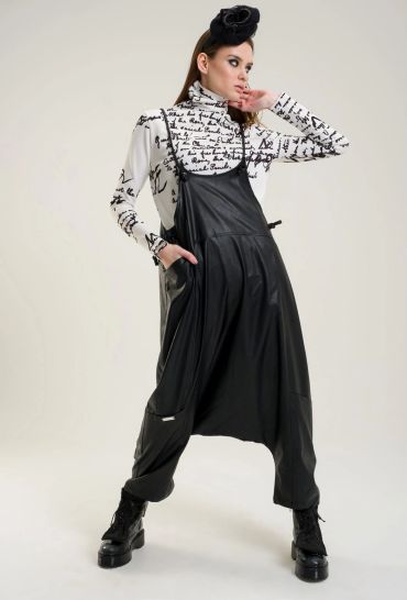 Model in black leather overalls and script print top with black boots and headpiece.