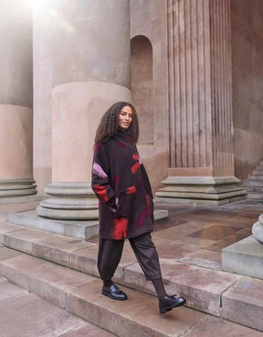 Woman in stylish outfit walking by large classical columns.