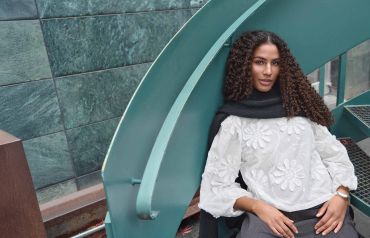 Woman with curly hair in white blouse and black scarf.