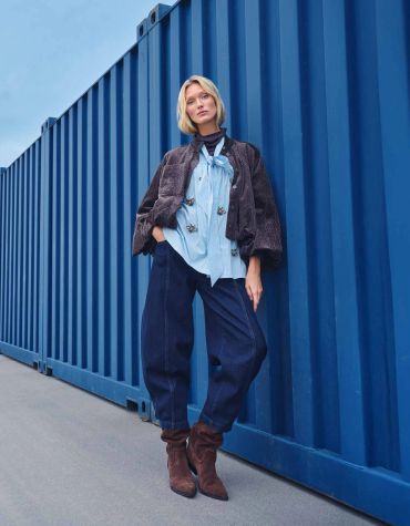 Woman stylishly posing against a blue container.