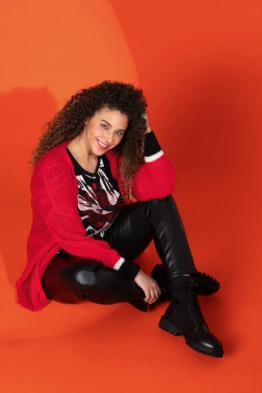 Smiling woman in red sweater sitting against orange background.