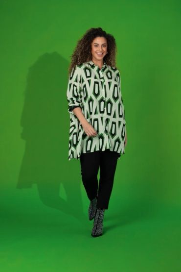 Woman smiling wearing patterned oversized shirt and black pants.