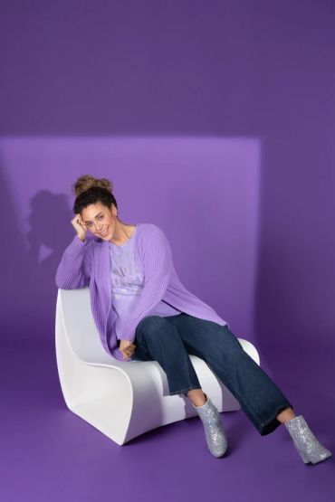 Woman in purple cardigan sitting on a white chair.