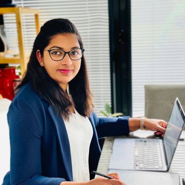 A woman in glasses working on a laptop and writing on a tablet.