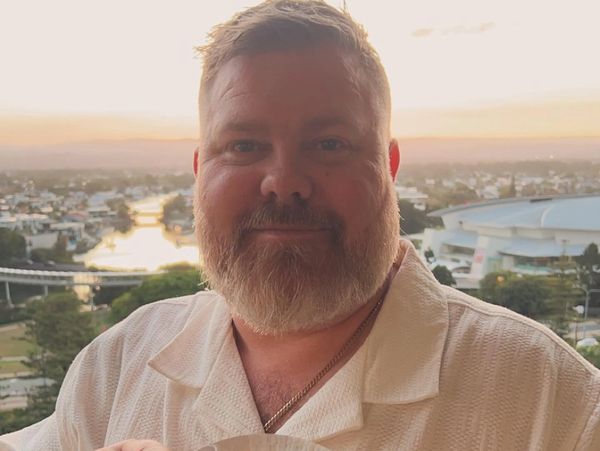 Smiling man with a beard in a white shirt at sunset overlooking a city landscape.