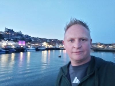 Man taking a selfie by the waterfront at dusk.