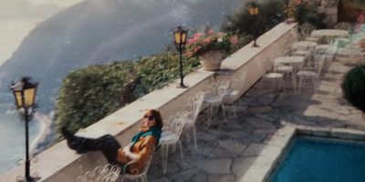 Person relaxing by pool on hillside patio with scenic view.