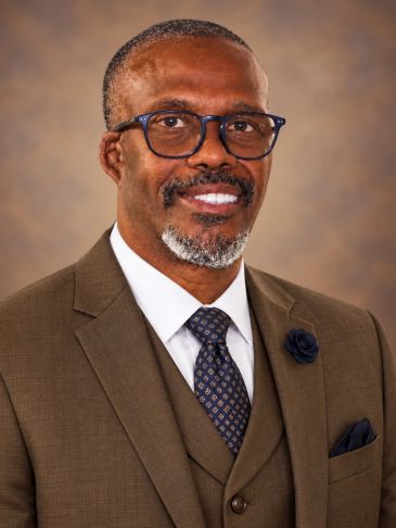 Professional portrait of a man in a brown suit.