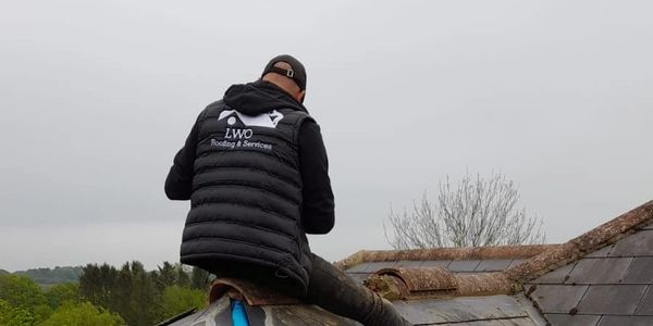 Worker inspecting a roof wearing LWO Roofing &amp; Services jacket.