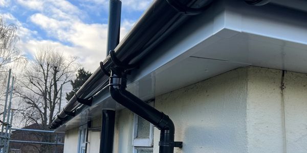 Close-up of black guttering on a white house against a cloudy sky.