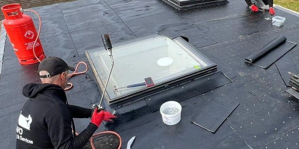 Worker applying roofing material around a skylight.