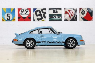 Blue vintage Porsche 911 parked indoors with racing number banners.