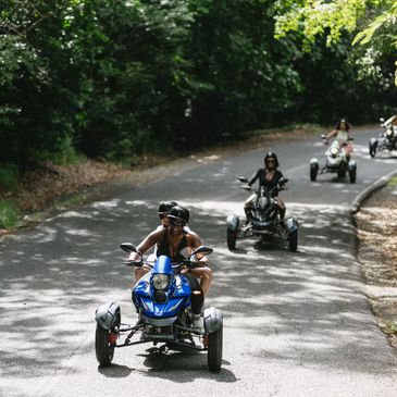 Group riding three-wheeled motorcycles on a sunny forest road.