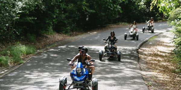 Group riding three-wheeled motorcycles on a sunny forest road.
