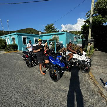 Group of four people with three-wheeled motorcycles in a sunny outdoor setting.